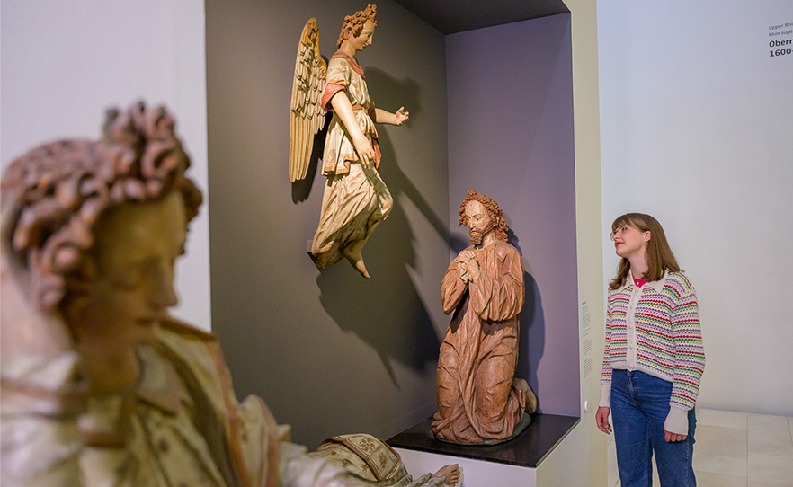 Eine Person betrachtet eine Ölbergszene, die aus fast lebensgroßen Holzskulpturen besteht.