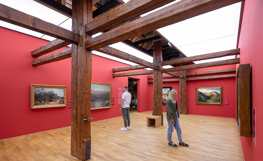 Zwei Personen betrachten Landschaftsgemälde in einem Galerieraum.